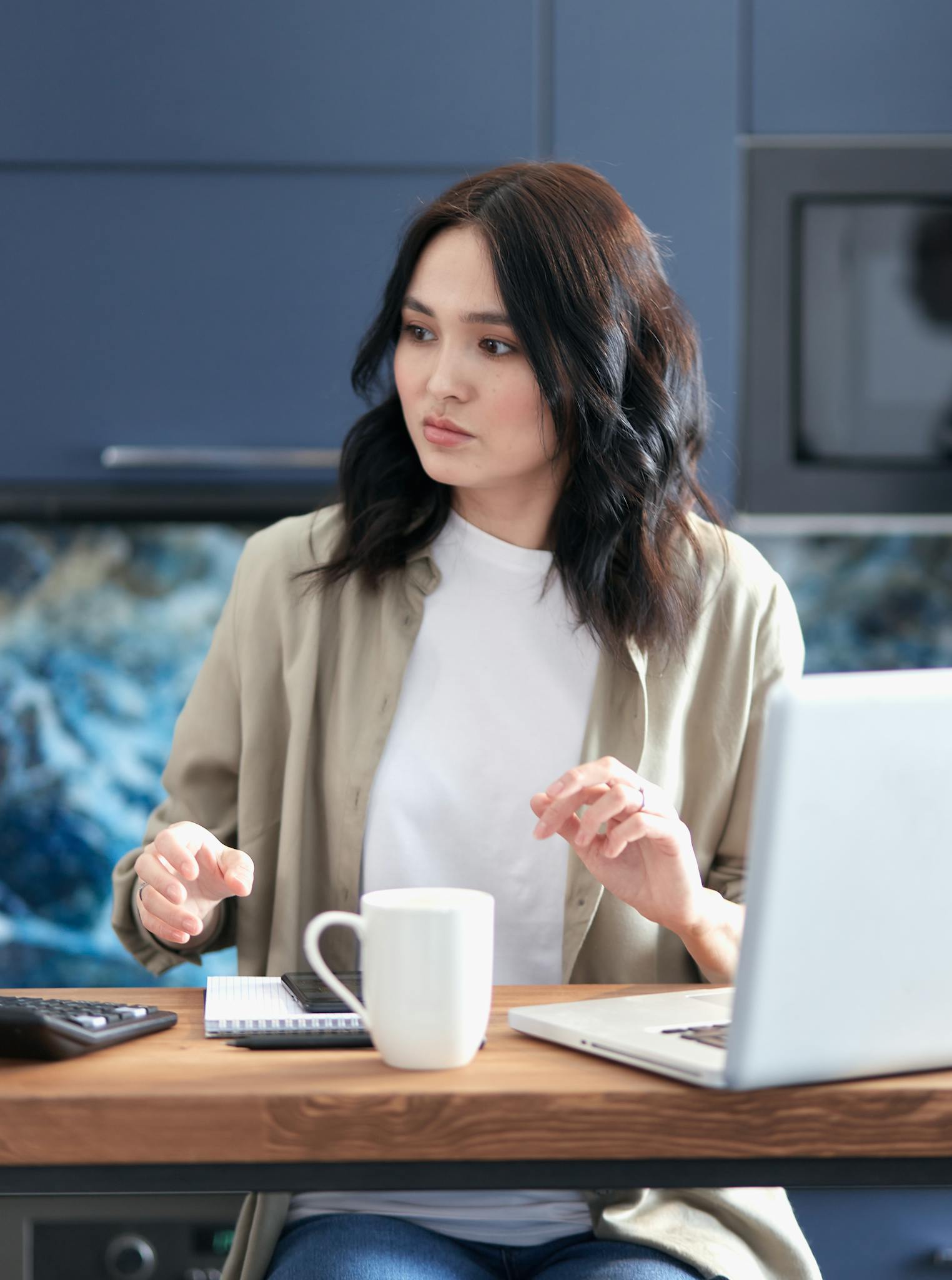 Focused young woman calculating budget while sitting with laptop and coffee at home.
